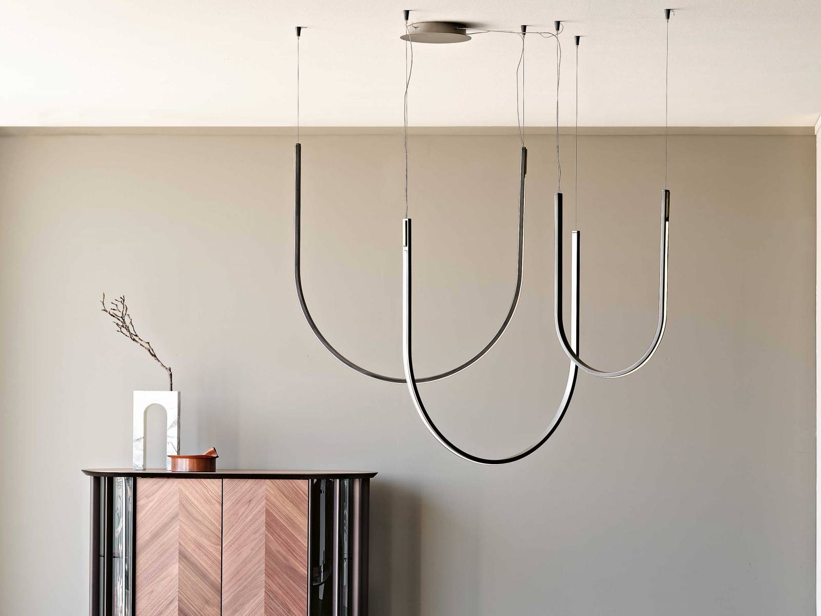 «Nahun» ist eine Komposition von Hängeleuchten, die es in zwei verschieden grossen Bögen gibt. Je nach Kombination und Anzahl der Bögen ergibt sich eine neue geometrische Form. Aus Stahl und Messing. Design: Studio Kronos. CATTELAN ITALIA.