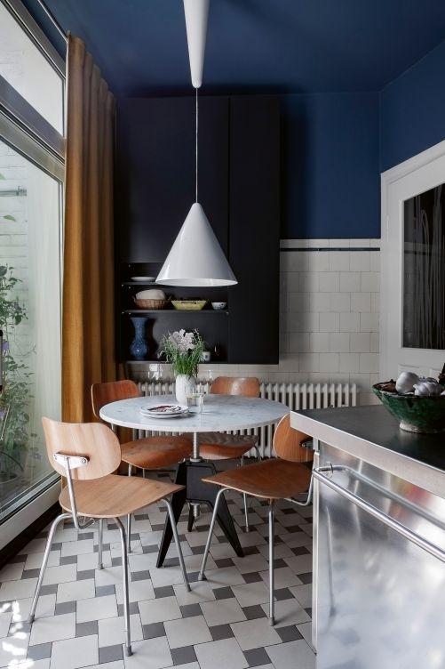 Die Küche befindet sich neben dem Mittelgang und wurde in einem ehemaligen Dienerzimmer eingerichtet. Die Wände sind in einem dunklen, warmen Blauton gestrichen und harmonieren mit den hellen Küchenmöbeln und dem Steinboden. Küchenstühle «SE 68» von Egon Eiermann, Tisch «Screw» von Tom Dixon, Hängeleuchte «Diabolo» von Flos.