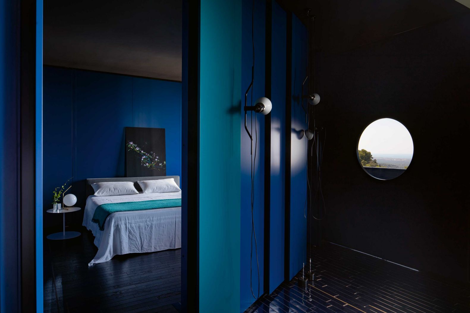 Blaue Stunden verbringt das Paar im stimmungsvollen Masterbedroom. Mit den dunklen Wänden und der ebenfalls blauen Decke wirkt er geradezu atmosphärisch. Nachtlicht: Flos; Bett: Lago Design.
